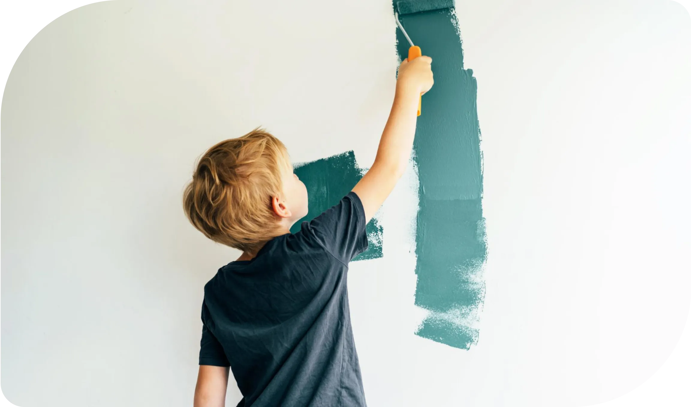 A young boy with blonde hair wearing a dark t-shirt is painting a white wall with a roller brush. The paint is a teal color, and he is reaching up to cover a section of the wall. A couple of teal paint strokes are visible on the wall. Representing home improvements