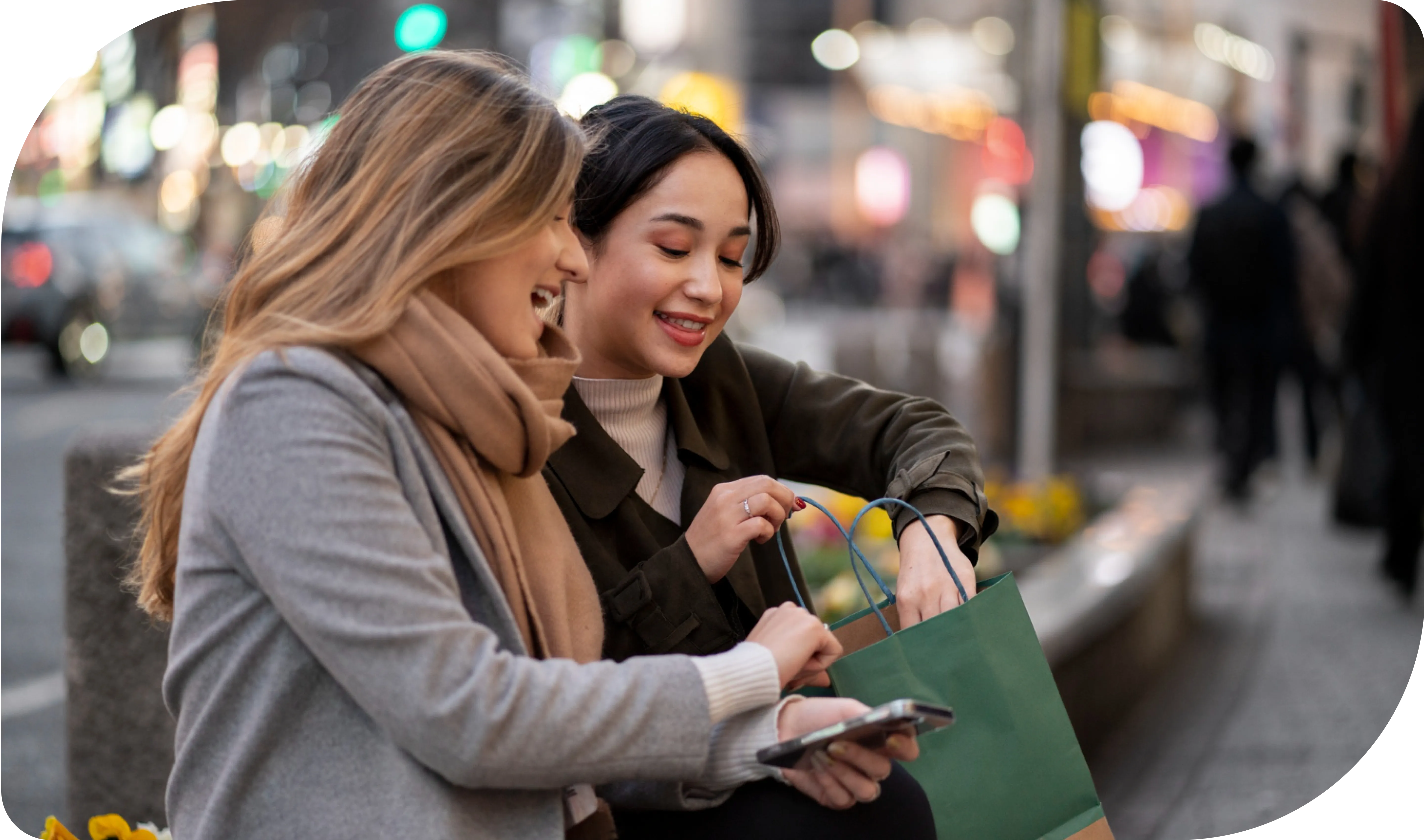 Deux femmes sont assises sur un banc de ville la nuit, l'une avec un sac de courses vert, l'autre souriant à côté d'elle. Représentant acheter sans soucis.